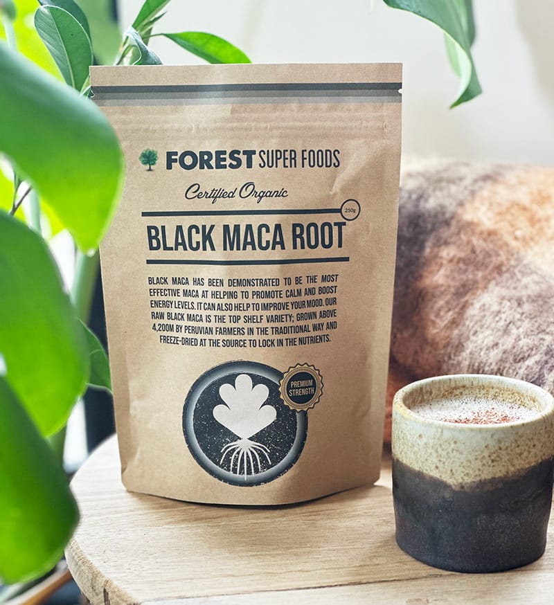 Forest Super Foods Certified Organic Black Maca Powder pouch displayed with a ceramic cup on wooden surface with plants nearby